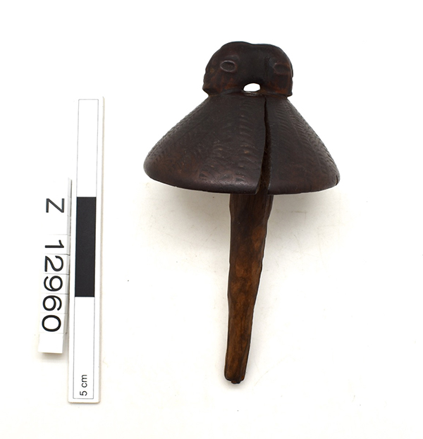 Carved wooden bottle stopper. Rounded top with two back to back heads and a long protrusion that narrows towards the tip. Large crack in the top.