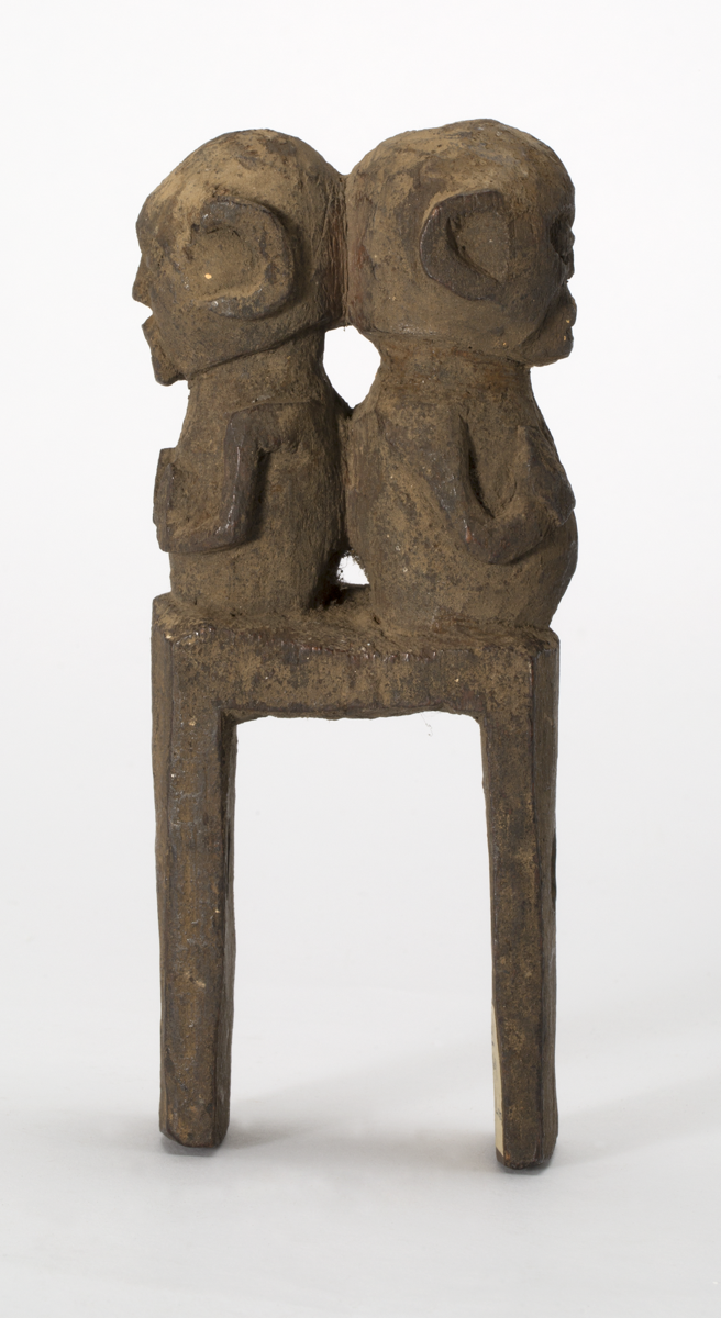 Loom attachment carved from wood. It consists of a wooden bracket with hole drilled through each arm for the loom string. On top of the bracket is two carved figures, one male and one female,back to back. 