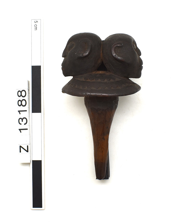Bottle stopper with rounded head, which has two back to back heads on it. Rounded top features carved zigzag decoration. Dark brown.