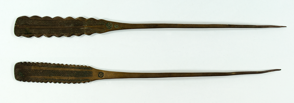 Two brass hairpins - one has jagged edges to its head, the other with much smaller, tiny jagged edges, decorated with spirals.