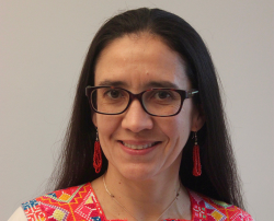 Dr Jimena Lobo Guerrero Arenas, smiling at the camera and wearing a Colombian-style printed top, brown glasses, and red earrings.