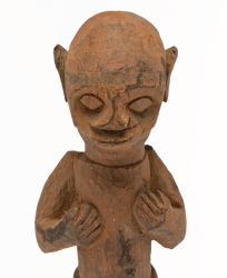Carved wooden figure. Male figure with short legs and a long torso, with hands resting on chest and knees slightly bent, stood on a round base. Reddish-orange pigment on surface.